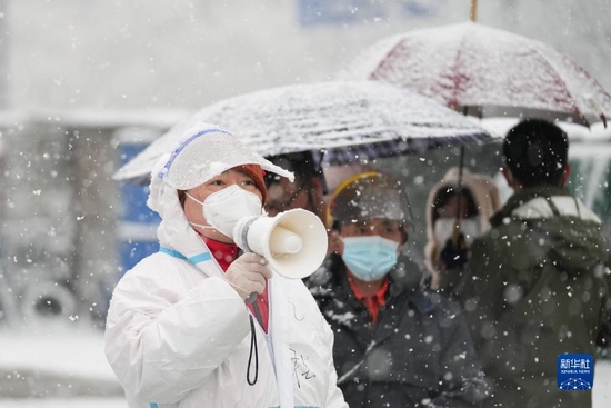3月18日，在北京市东城区北新桥街道一处核酸采样点，工作人员冒雪引导前来检测的居民。新华社记者 鞠焕宗 摄